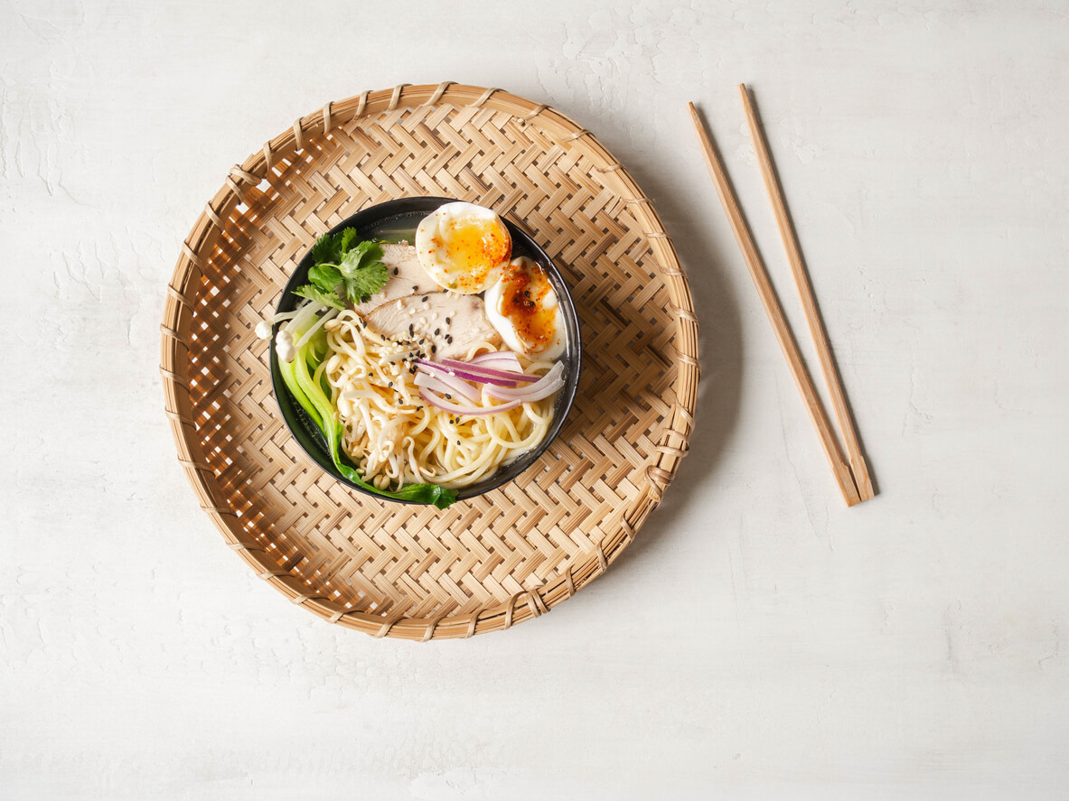 Chicken ramen noodle soup with meat, bok choy, mushrooms, egg in black bowl on grey background.