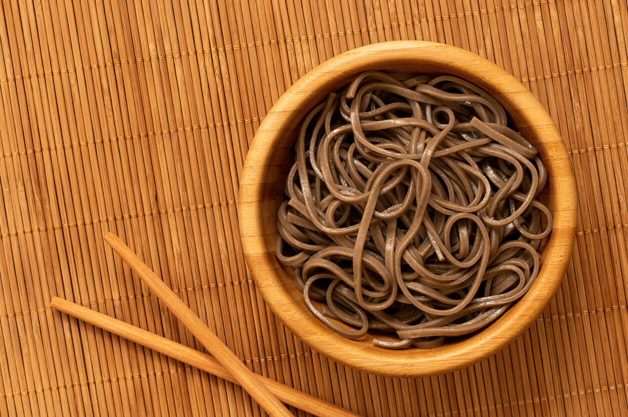 Cooked soba noodles in a bamboo bowl on a bamboo matt.