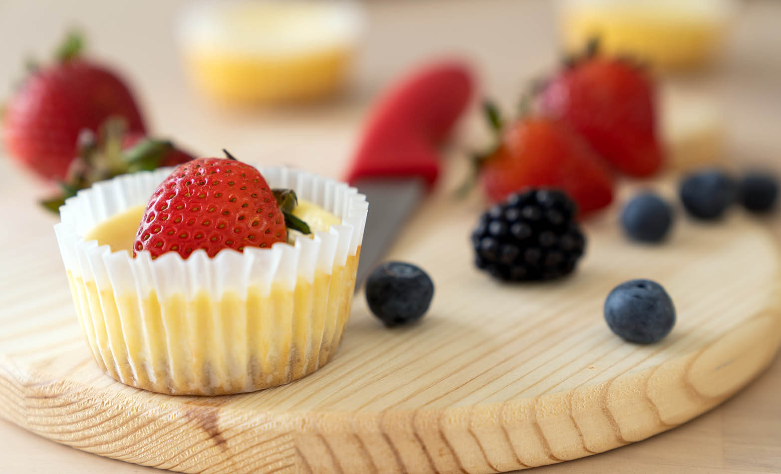 a mini cheesecake cup topped with a strawberry and surrounded by berries