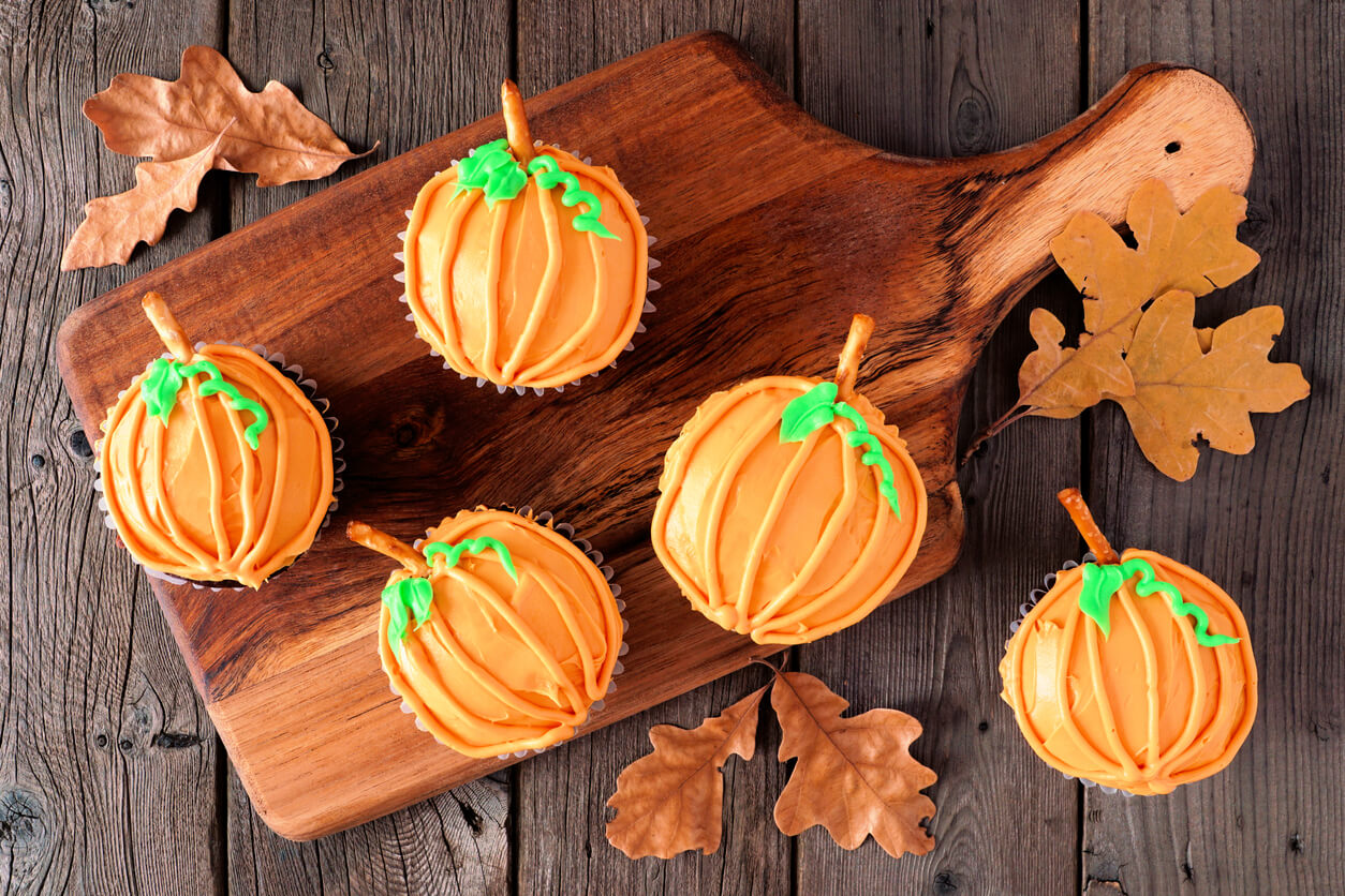 Autumn pumpkin cupcakes on a wooden serving platter over rustic wood