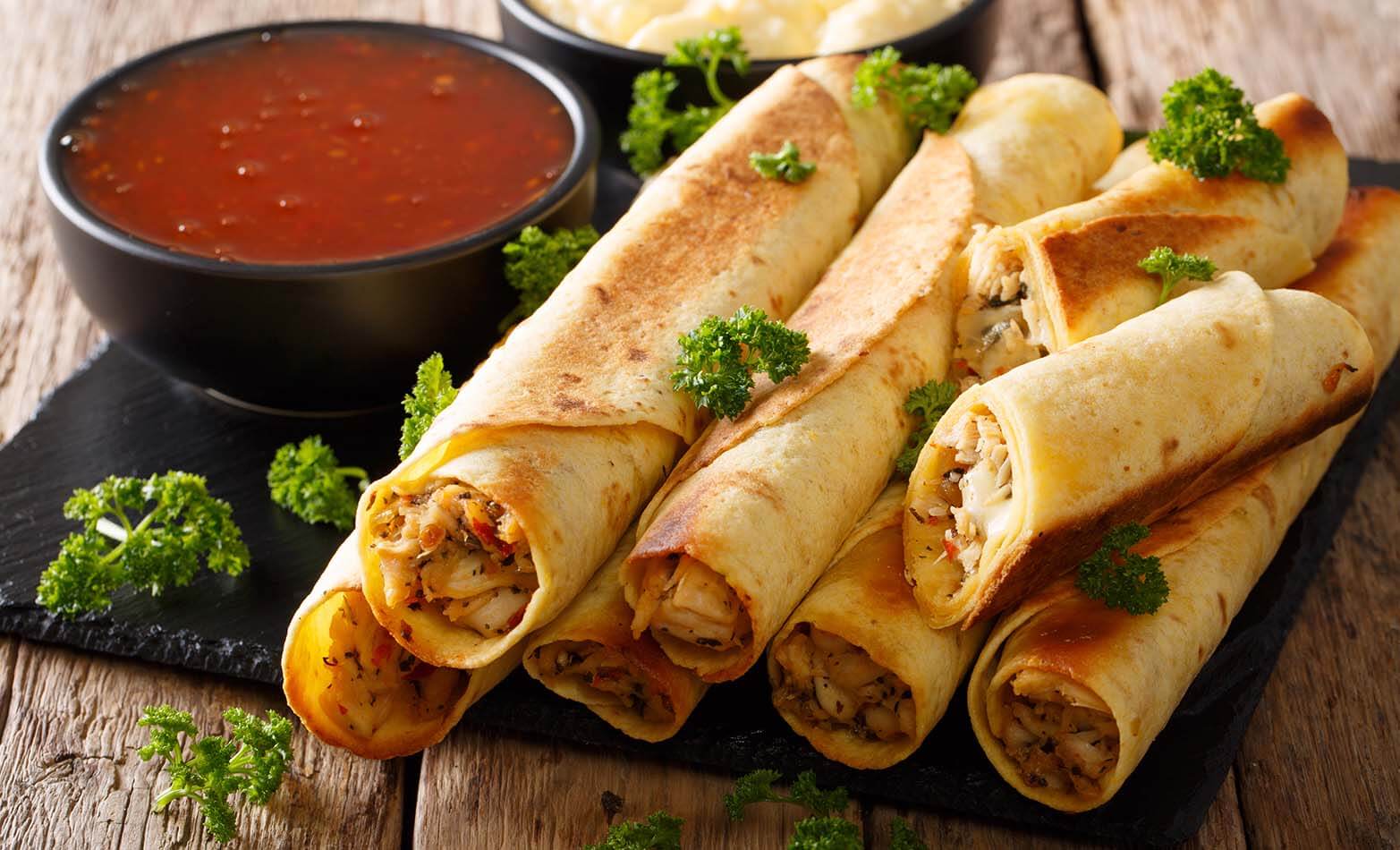 a platter of chicken taquitos with a side of red sauce