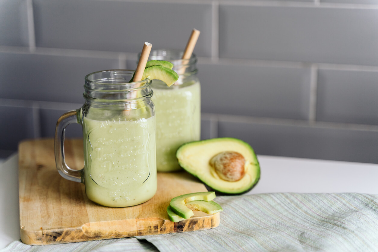 creamy smoothie from avocado and banana in glass cups with paper tubes on a light background.