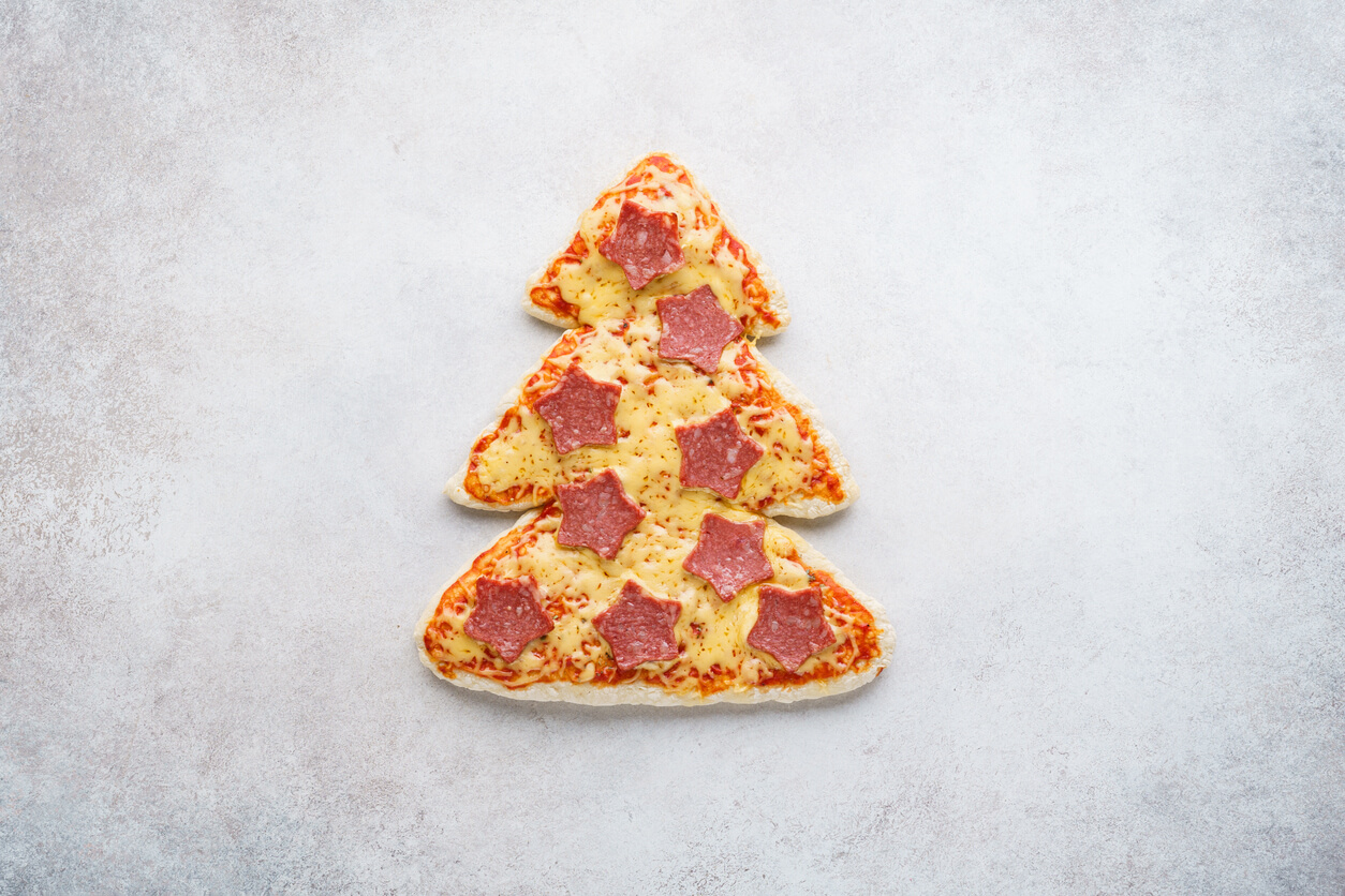Pizza shaped as Christmas tree decorated with stars made of pepperoni.