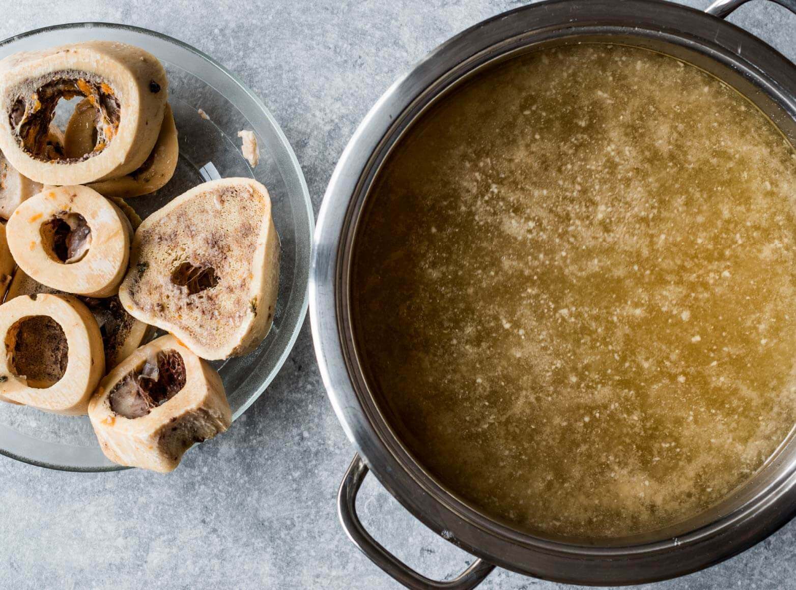 Overhead view of a simmering pot of stock and meat bones in a bowl next to it
