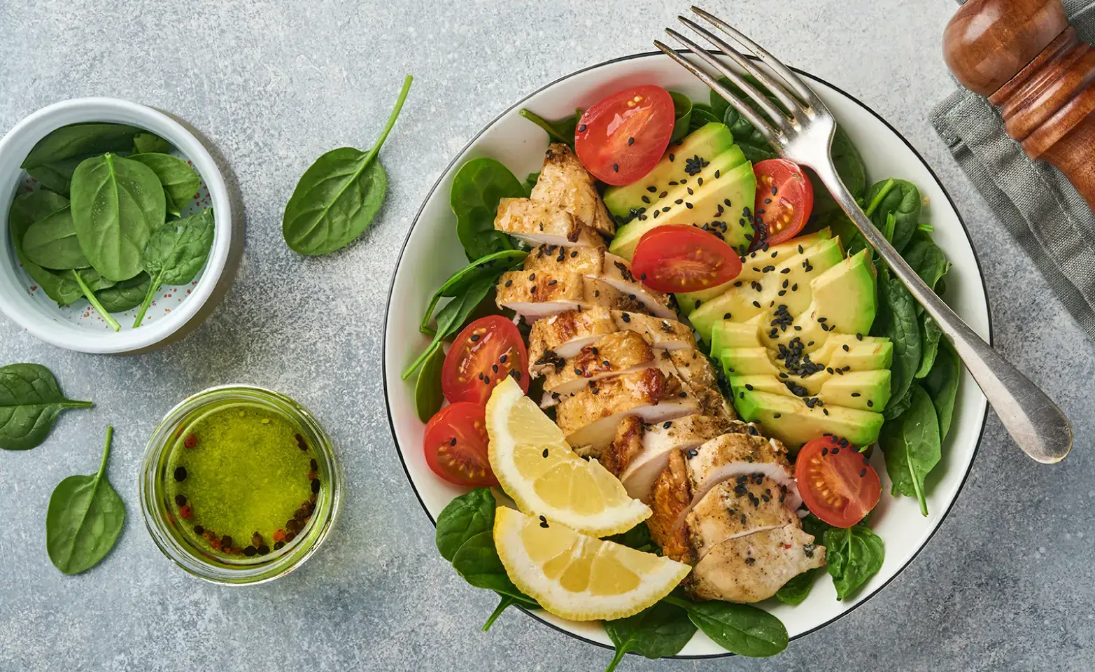 Chicken keto salad with spinach, tomatoes, avocado and lemon wedges