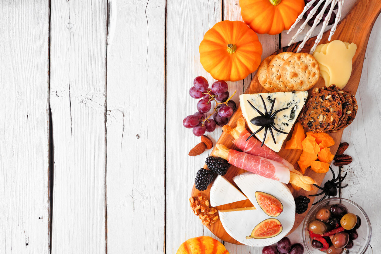 Halloween theme charcuterie side border against a white wood background. Selection of cheese and meat appetizers. Copy space.