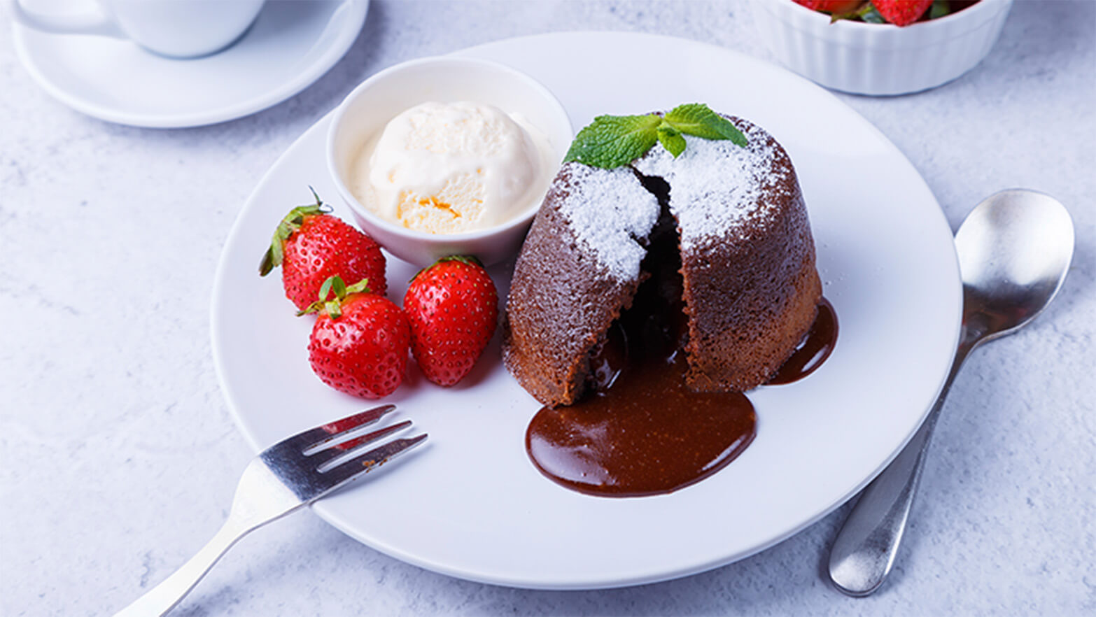 Chocolate lava cake on plate with strawberries and a bowl of ice cream.