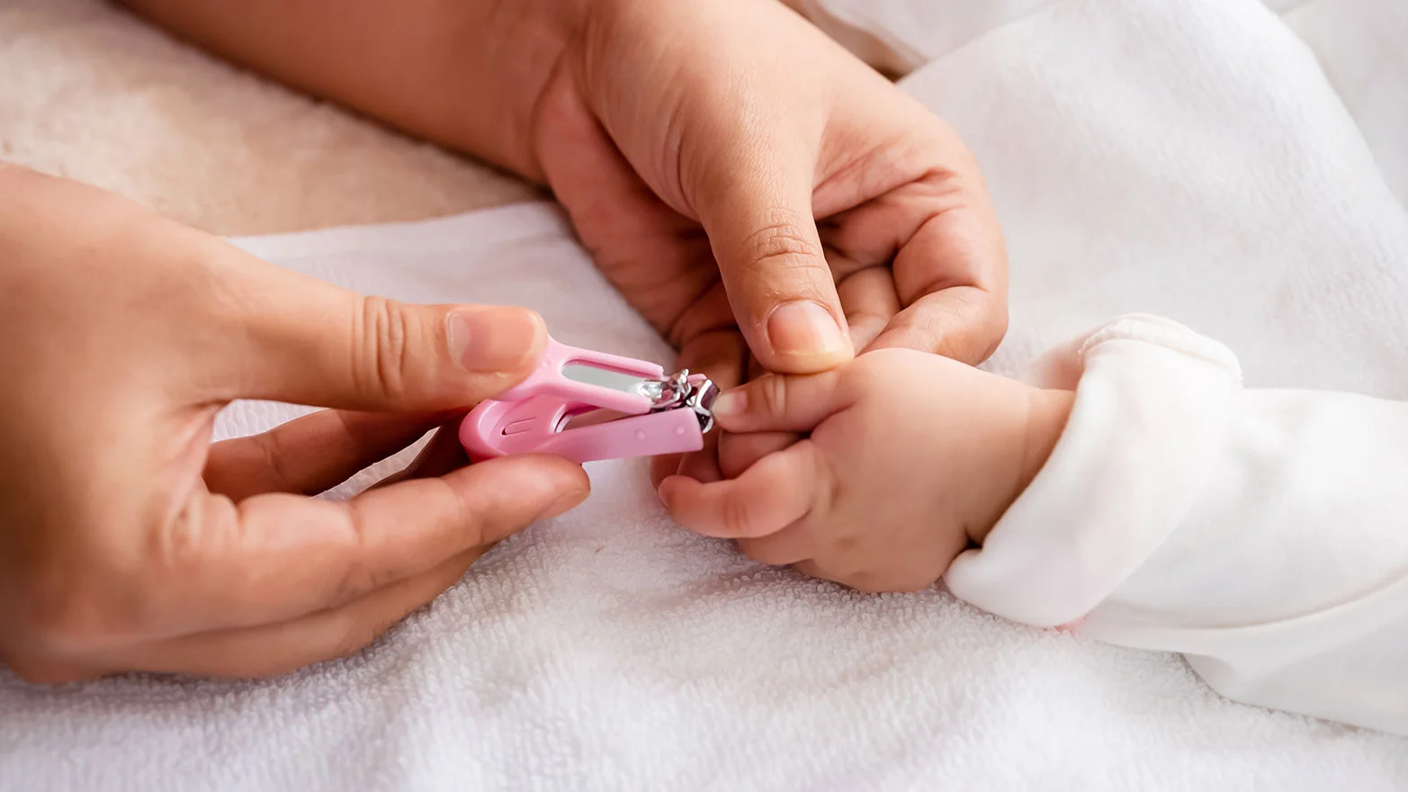 A close-up stock photo of a baby’s hand getting nails clipped with pink nail clippers.