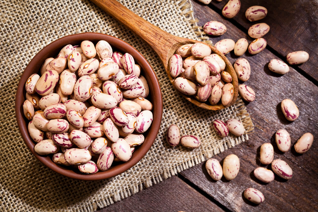 Top view of a brown bowl filled with pinto beans shot on rustic wood table.
