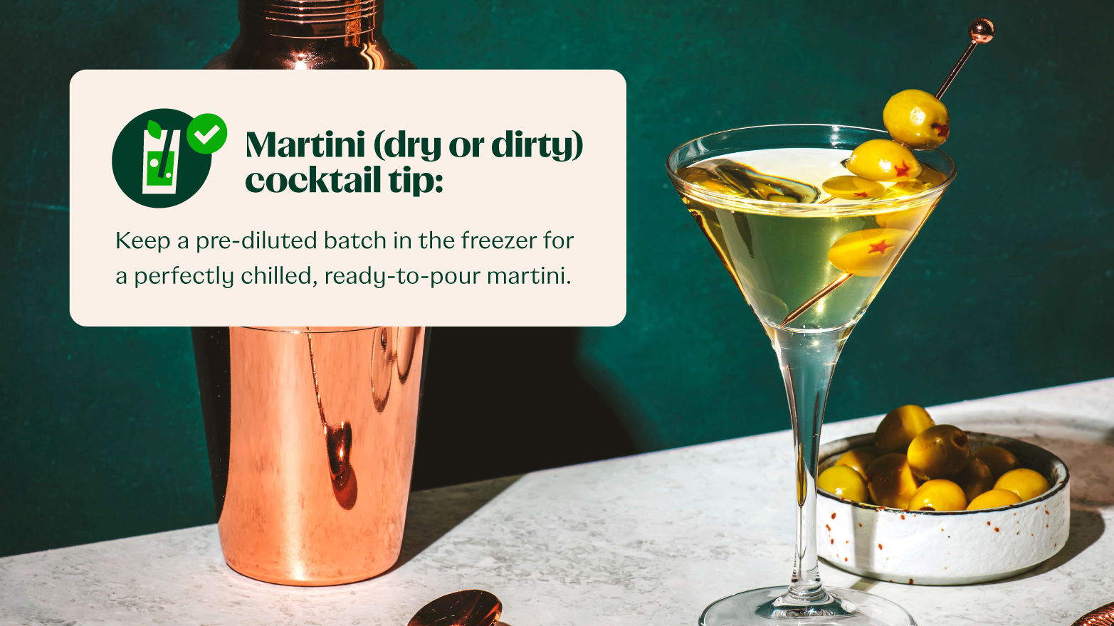 a martini in a glass next to a shaker and a bowl of olives