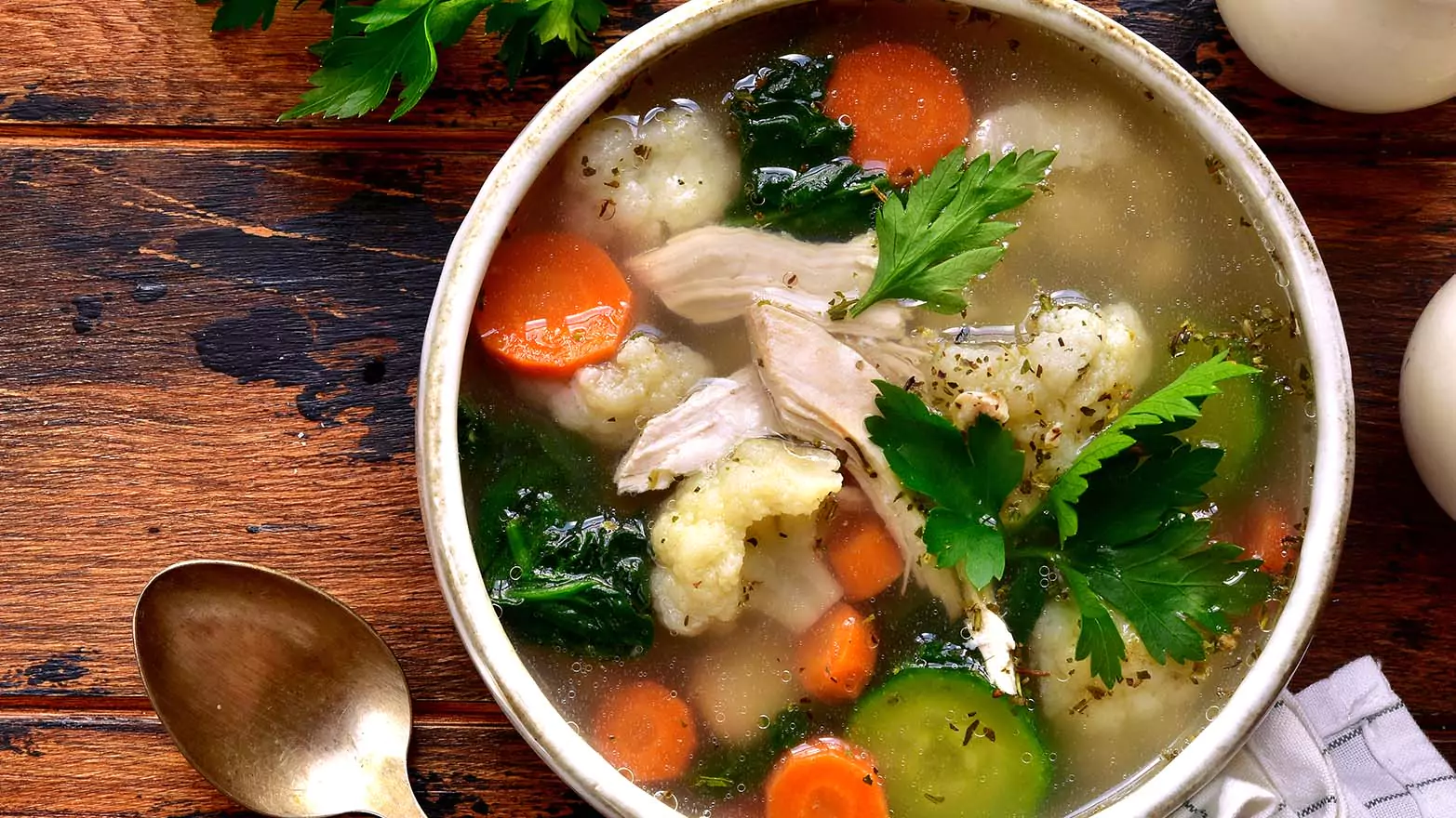 A bowl of clear soup on a wooden table.