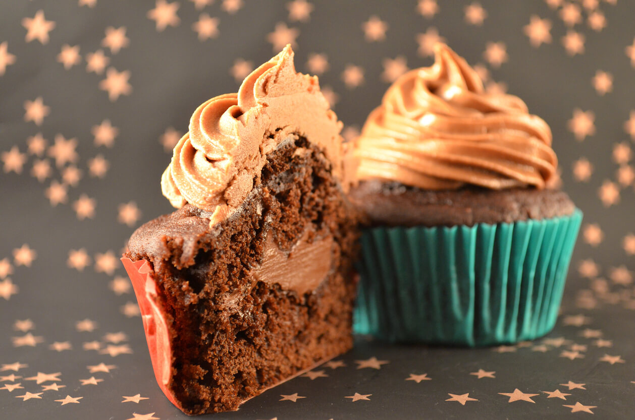 two chocolate cupcakes filled chocolate cream with chocolate icing in colorful paper case.