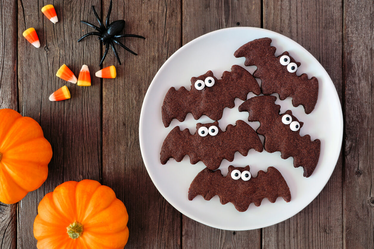Chocolate Halloween bat cookies. Above view with decor on dark wood.