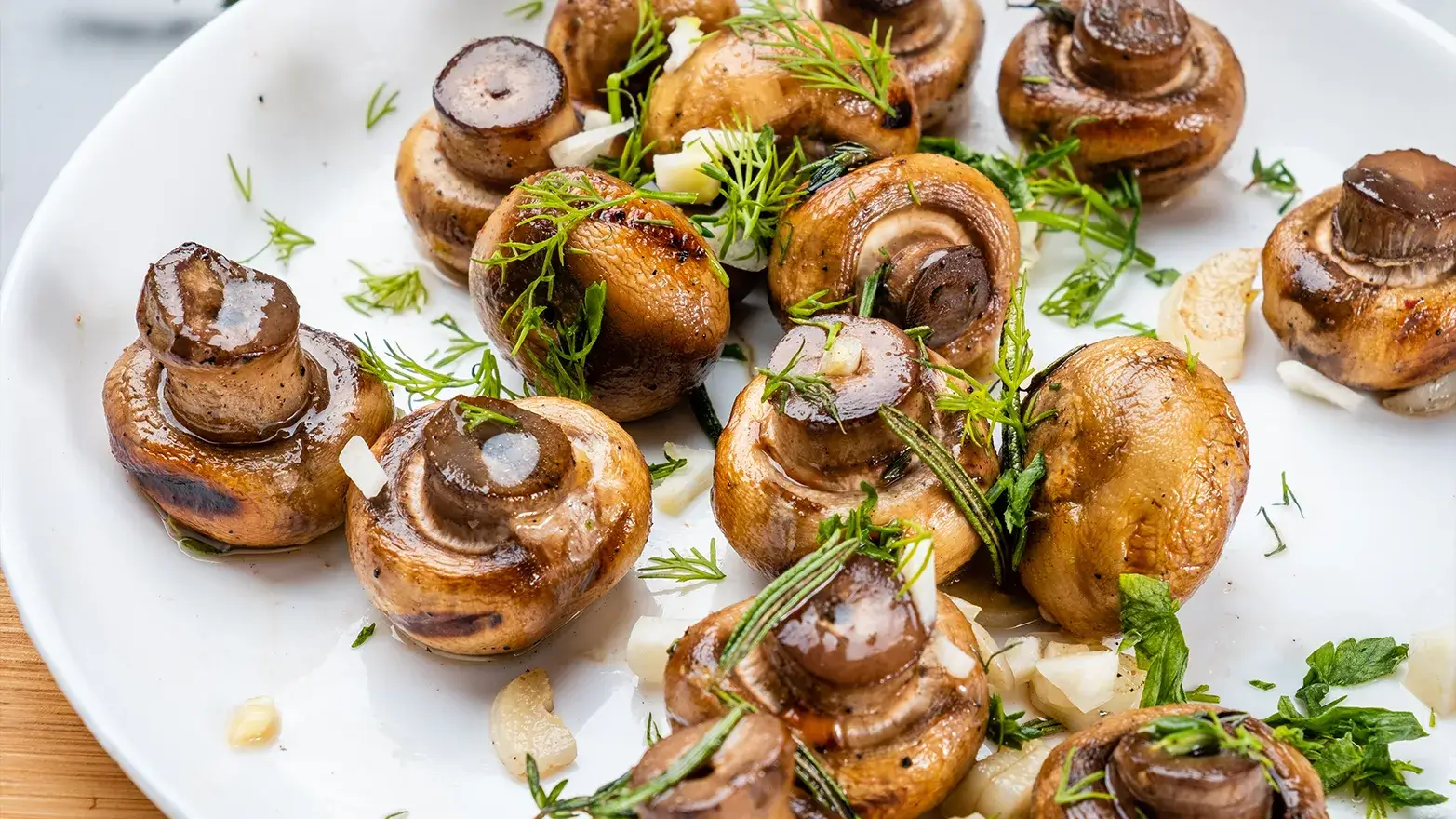 Roasted button mushrooms with herbs on white plate.
