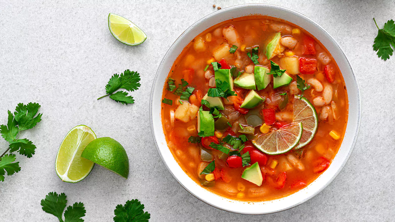 A bowl of traditional posole soup with lime wedges.