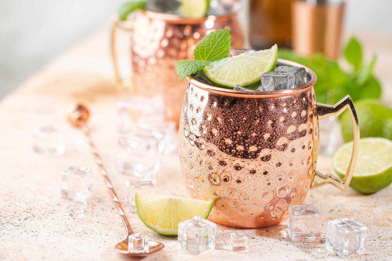 Cold Moscow Mules cocktail with ginger beer, vodka, lime. White stone background.