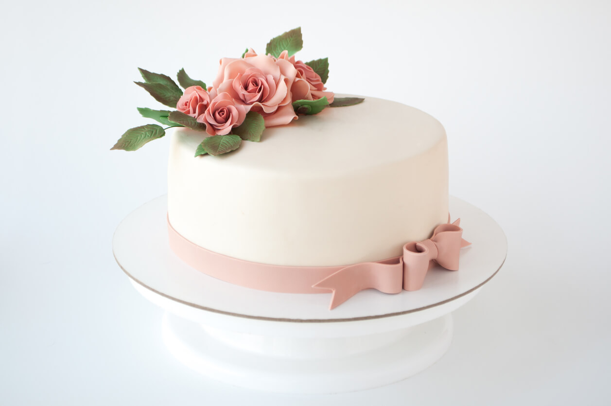 Art cake decorated with pink flowers and green leaves from mastic on a white background.