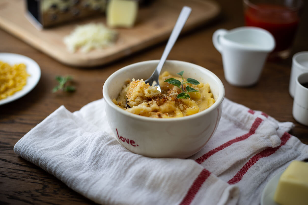 Homemade Baked Mac and Cheese on a Wooden Table with Ingredients Placed Around it.
