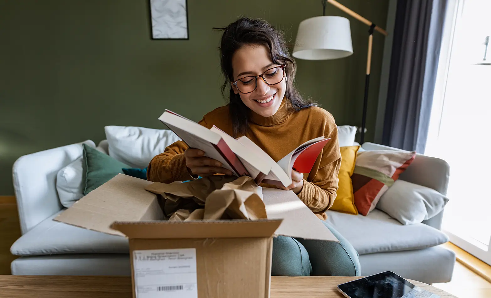 A photo of a smiling woman unpacking a box of books.