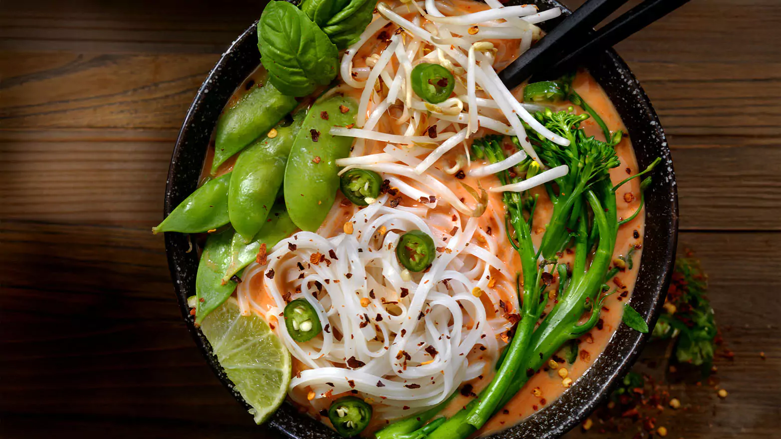A bowl of rice noodle soup on a wooden table.