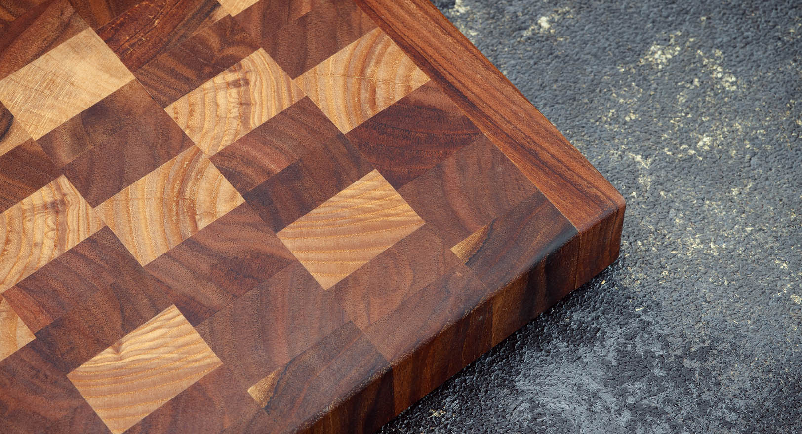 A close-up photo of a wooden cutting board with a checkered pattern.