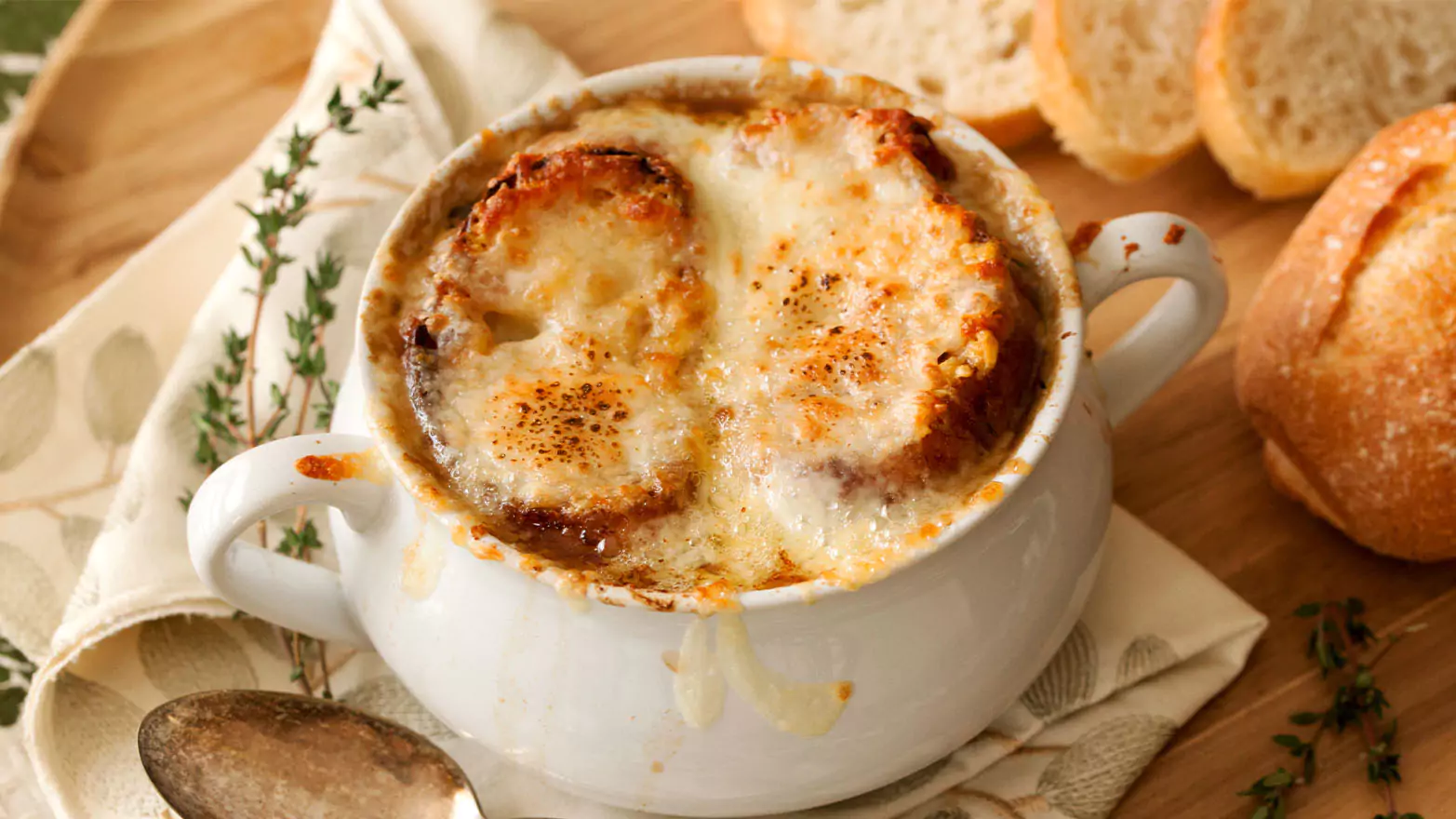 A bowl of French onion soup served with a sliced baguette.
