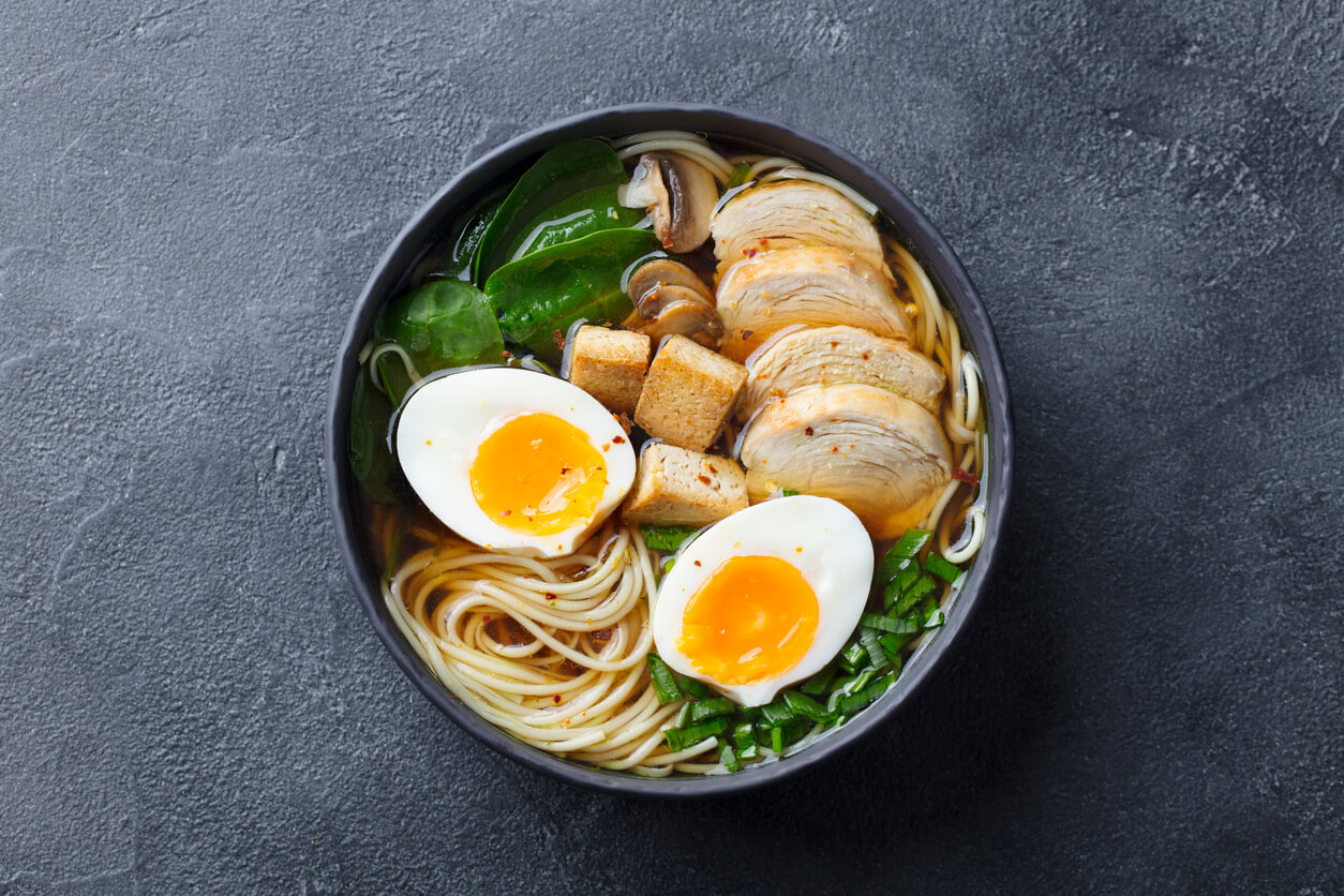 Asian noodle soup, ramen with chicken, tofu, vegetables and egg in black bowl. 