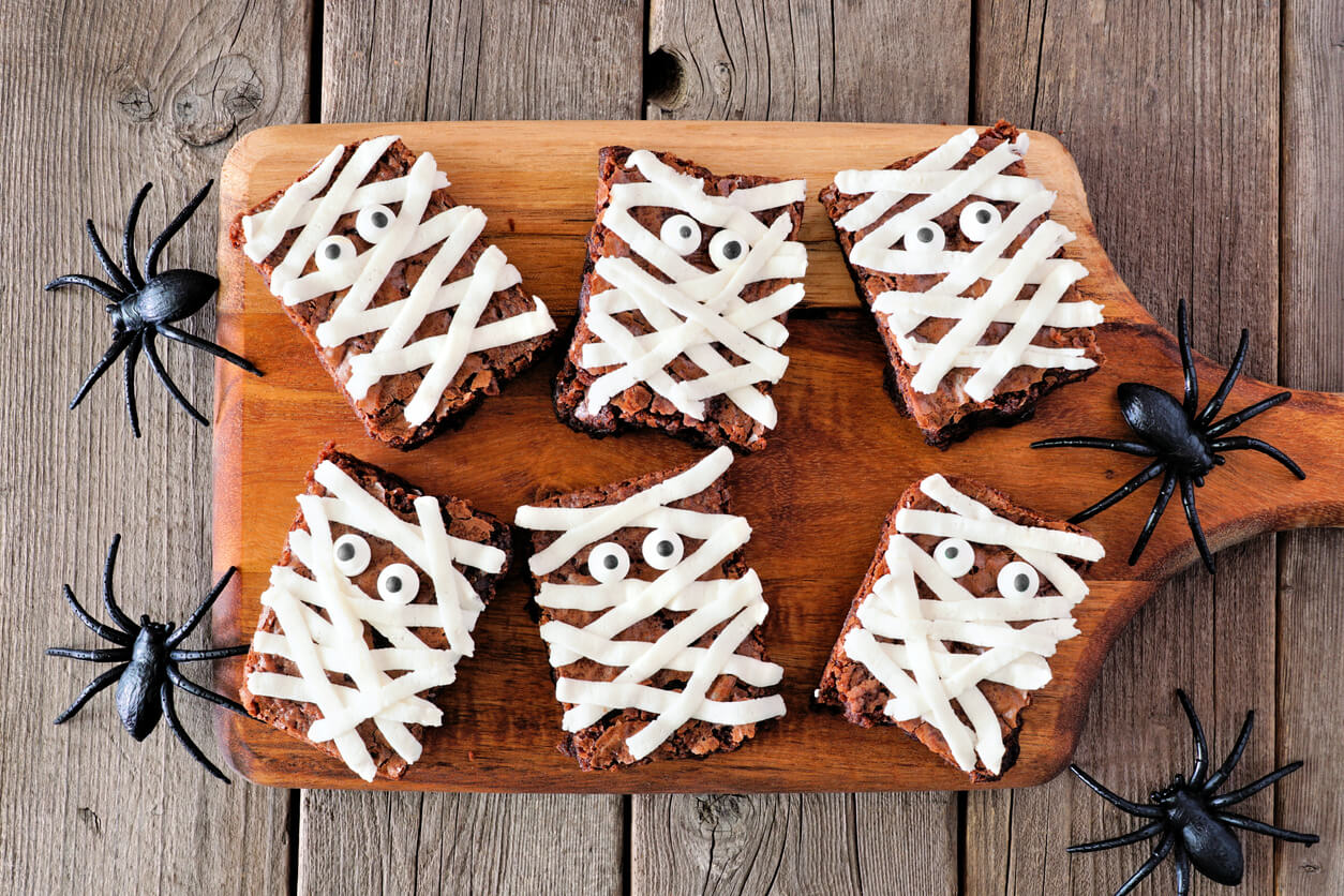 Halloween mummy brownies, top view with spiders on a serving board with a wood background