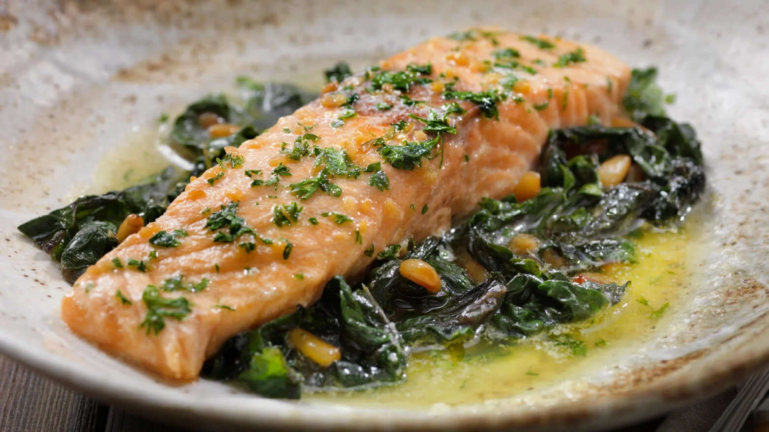 a photo of steamed salmon with lemon herb sauce on a bed of spinach