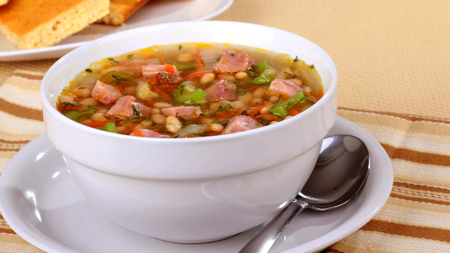 A bowl of ham and bean soup served with cornbread.