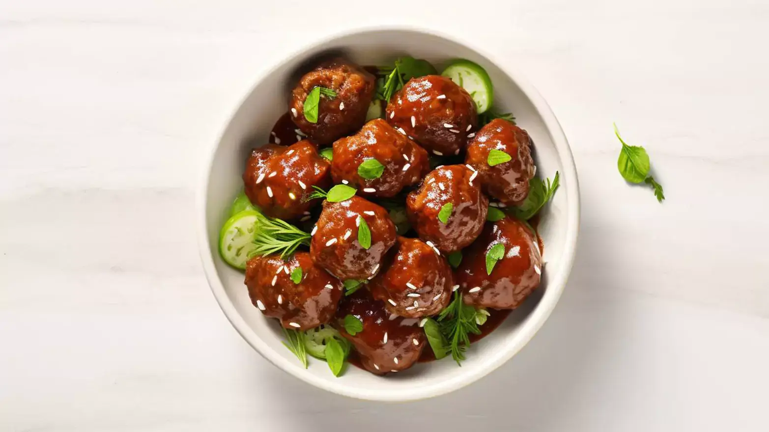 White bowl of Swedish meatballs with herb garnishes on a white countertop