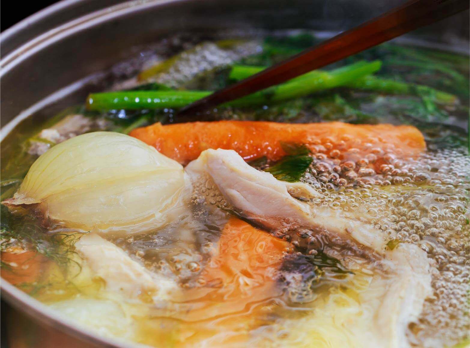 Simmering pot of broth with chicken meat onions and carrots