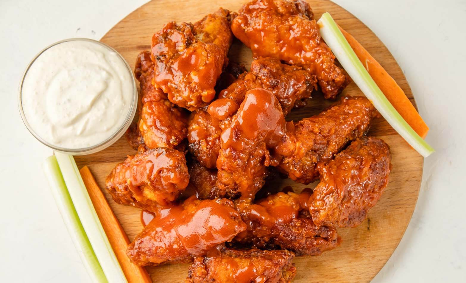 a pile of classic buffalo wings served with veggies and ranch dipping sauce