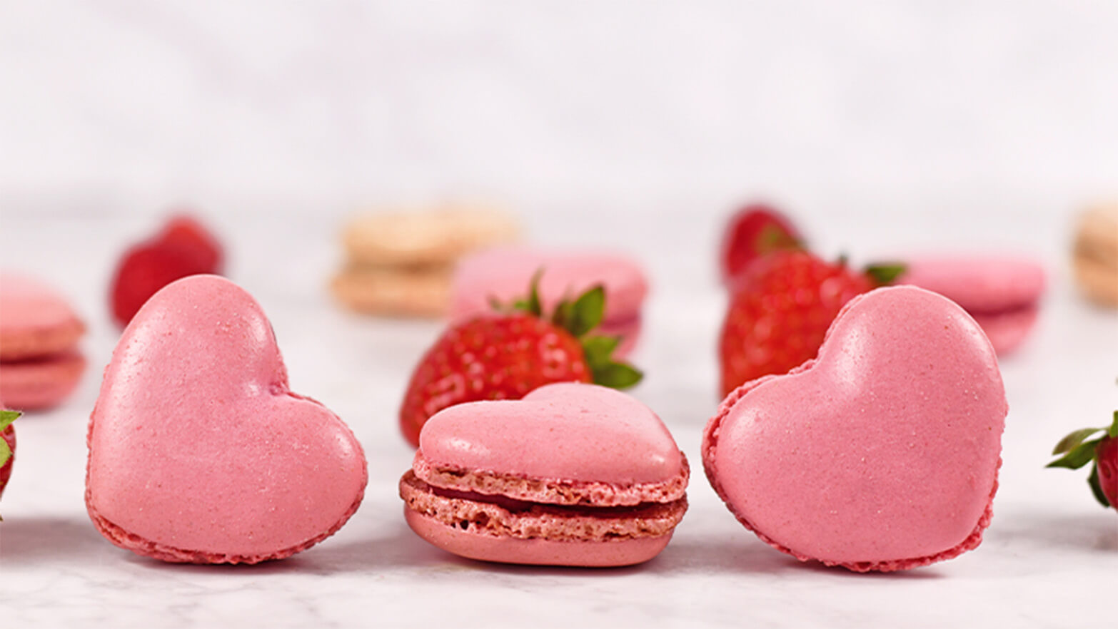 Assortment of French macarons shaped like hearts with strawberries.