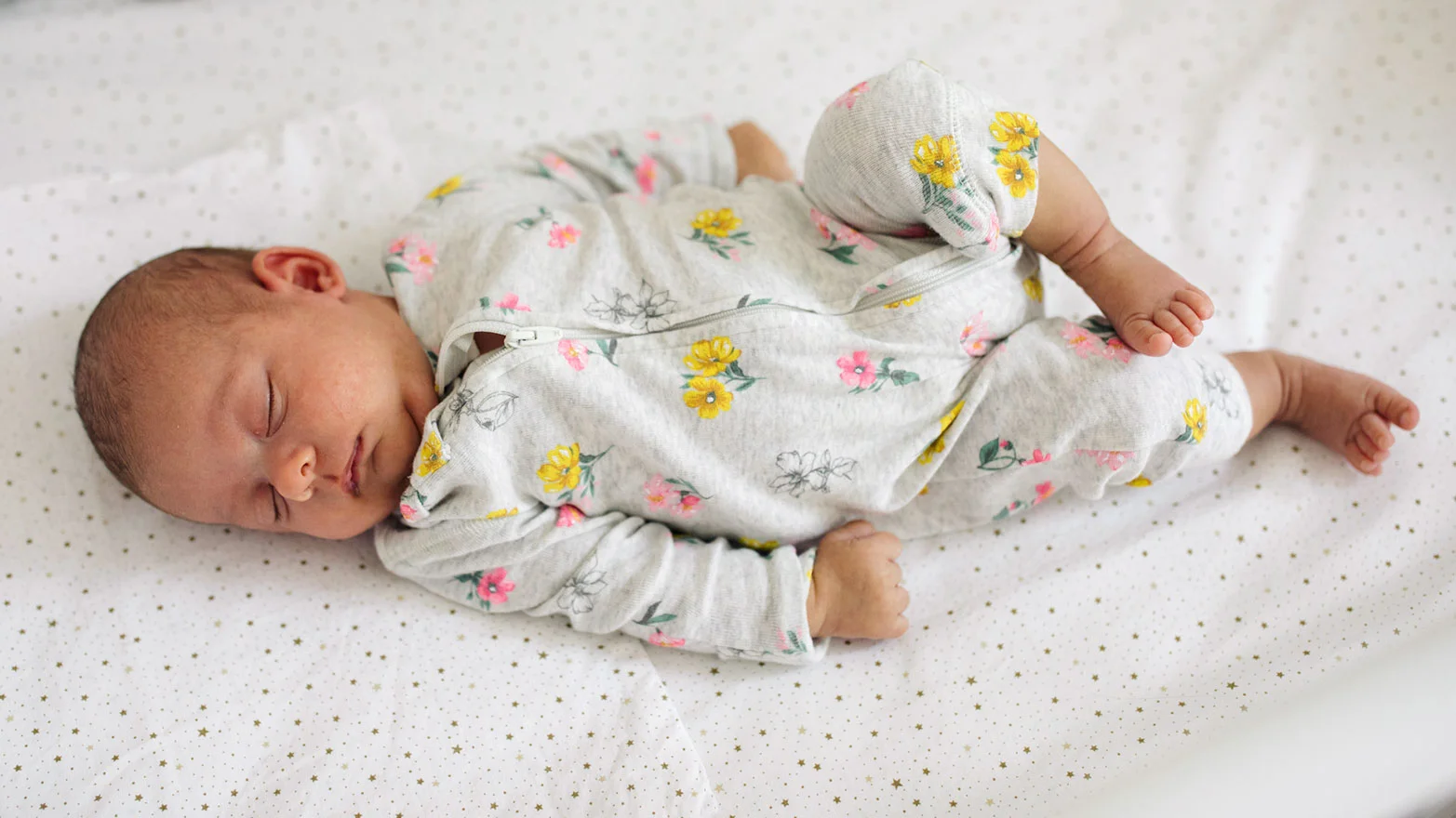 A stock photo of a baby wearing floral zip-up onesie pajamas.