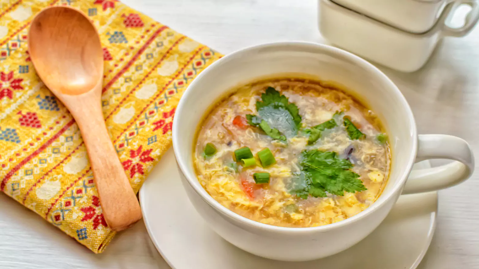 A bowl of egg flower soup with a wooden spoon and a colorful napkin.
