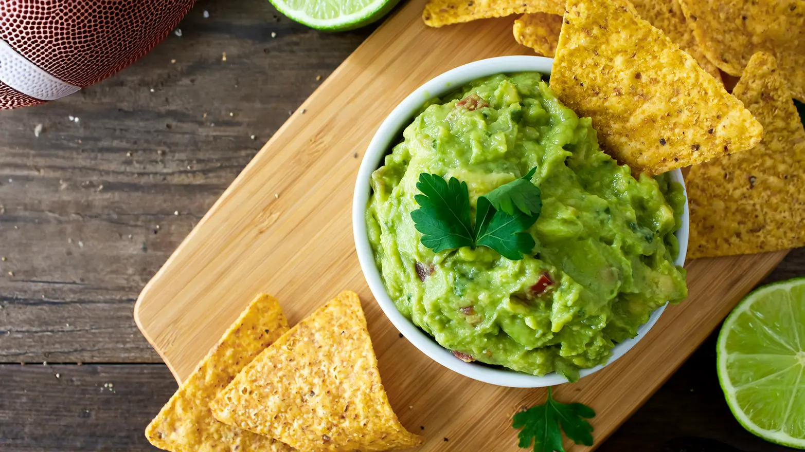 Guacamole and tortilla chips staged on a wooden board with a football.