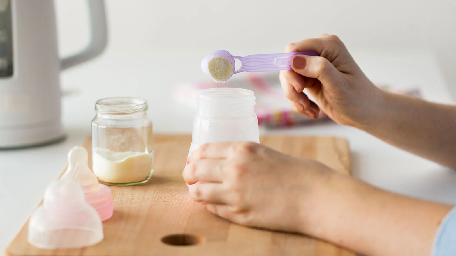 A stock photo of someone’s hands preparing a scoop of baby formula powder in a bottle.