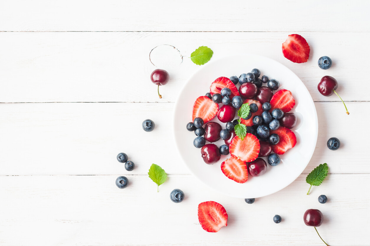 Fruit salad with strawberry, blueberry, sweet cherry on wooden white background.