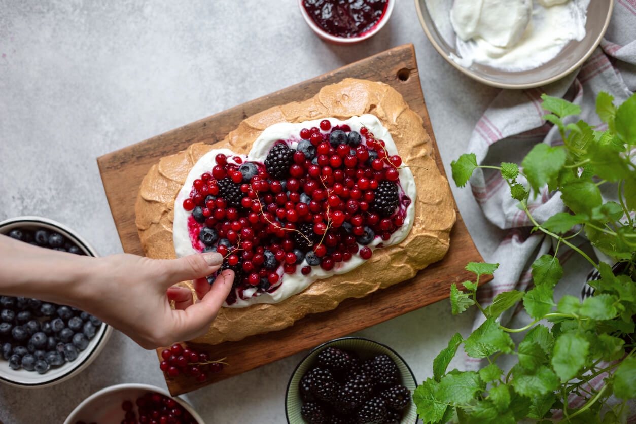 Preparing Berry Pavlova Cake with blueberry, blackberry and red currant.