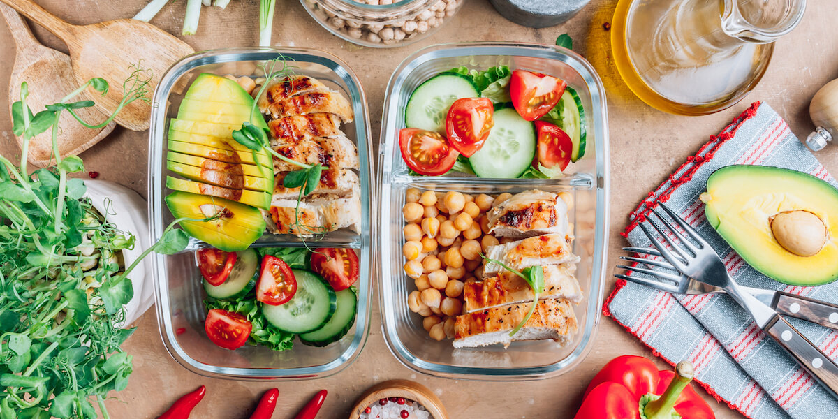 Healthy meal prep containers with chickpeas, chicken, tomatoes, cucumbers and avocados.