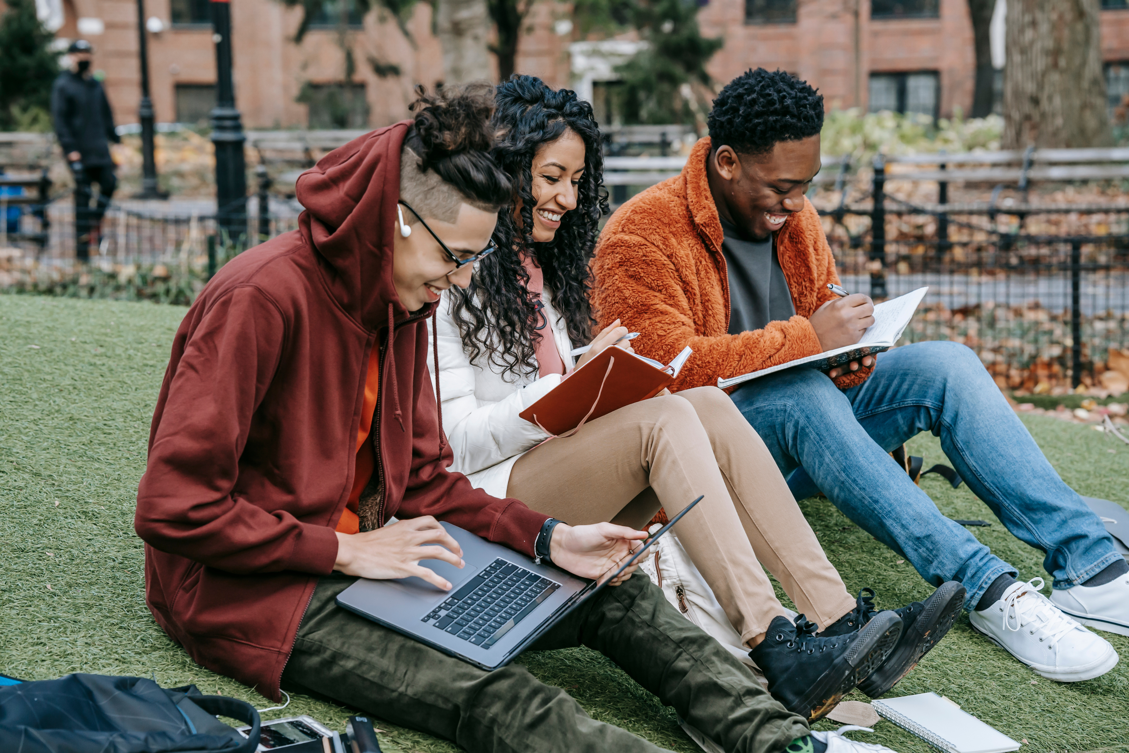 studenci uczą się angielskiego na dworze, patrzą w książki, laptopa i uśmiechają się