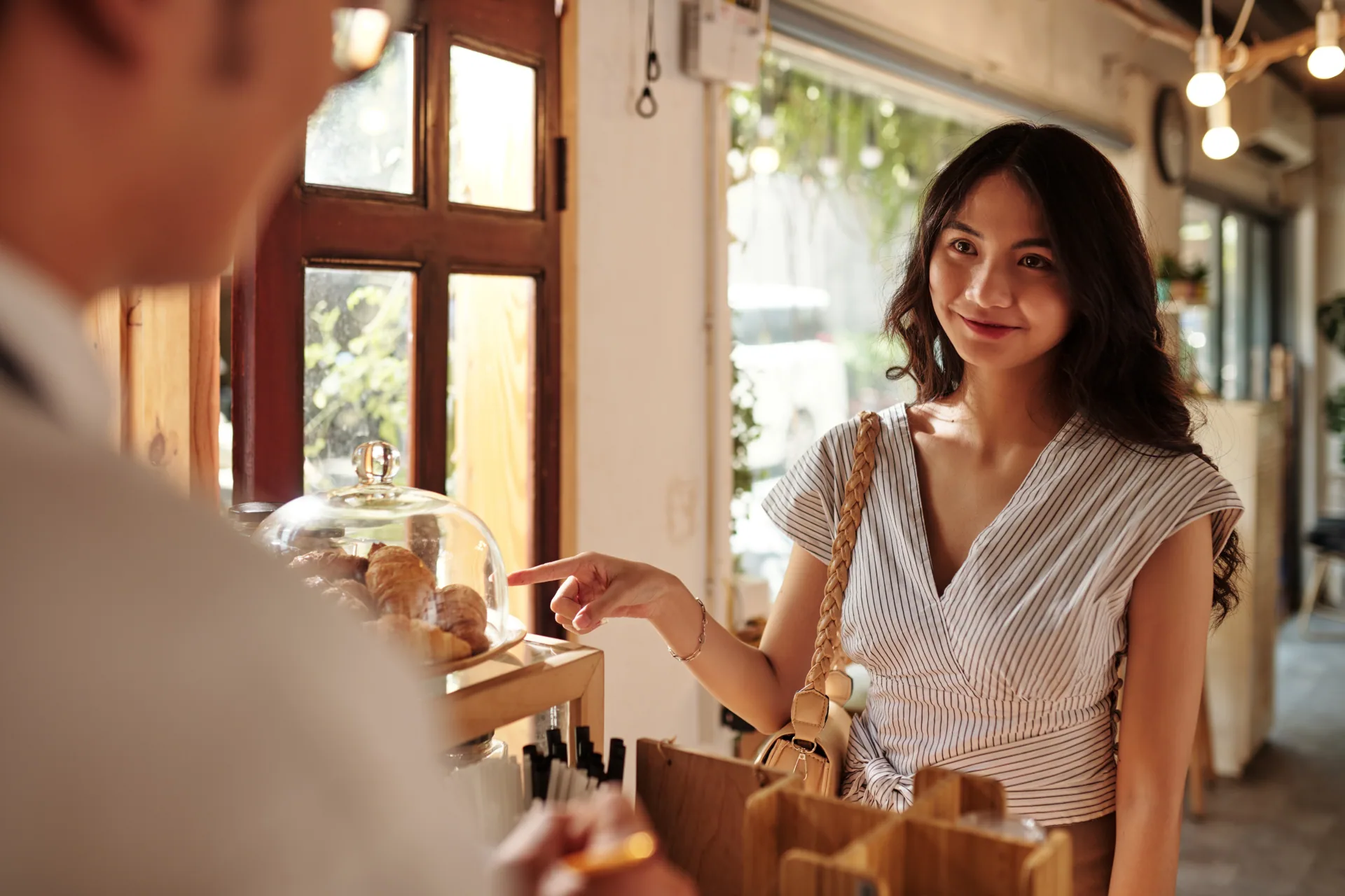 Woman in a bakery pointing at some pastries and also asking for her favoire coffee
