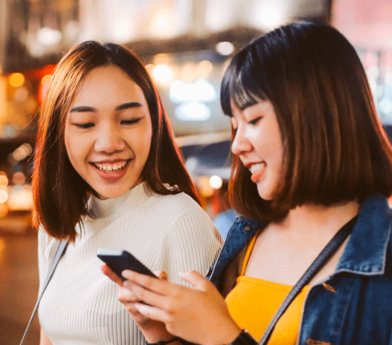 Two young Asian women looking at a cellphone