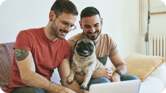 Two men with their dog looking at a laptop