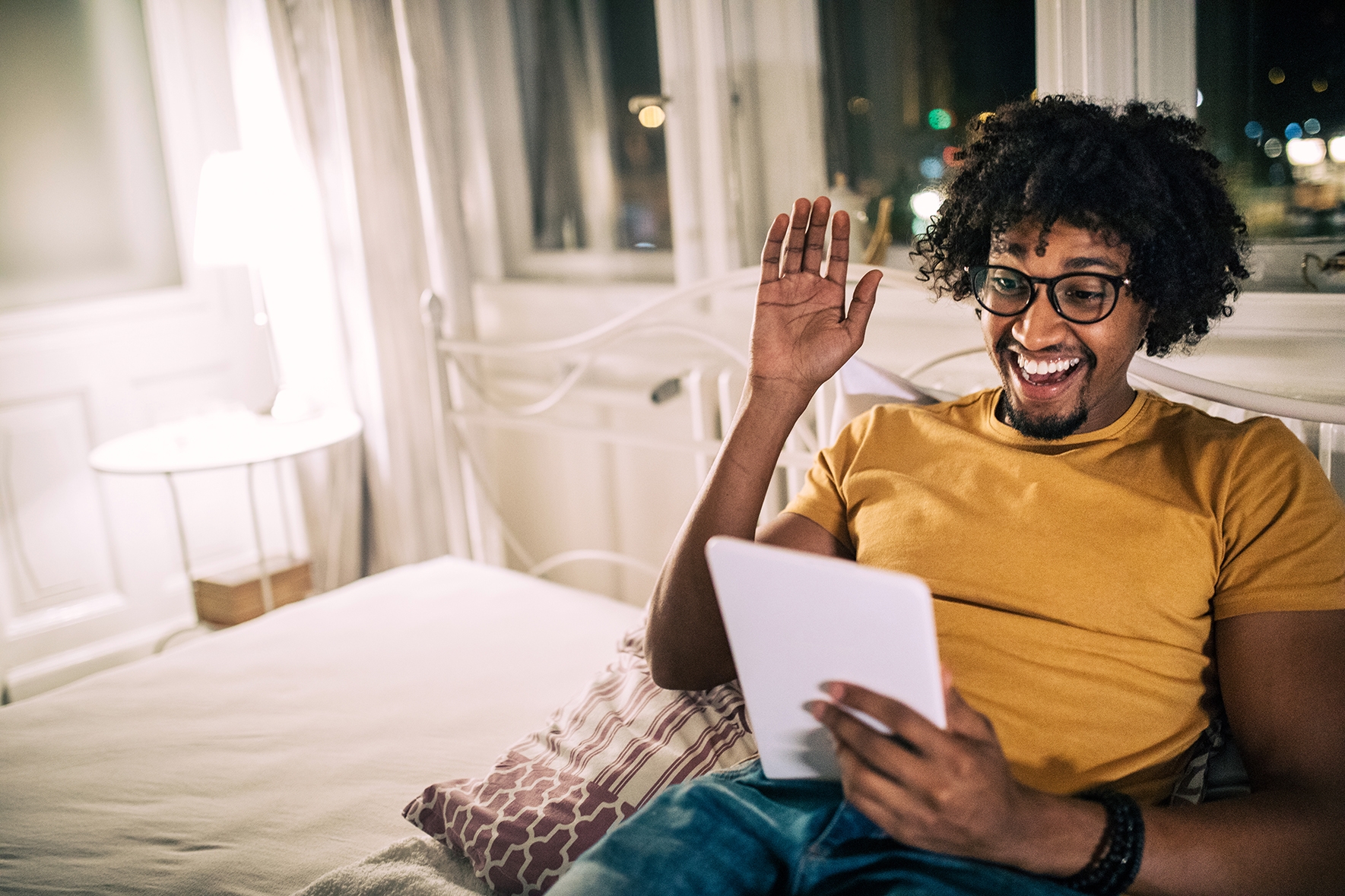 Man holding a tablet and waving at his instructor at the beginning of his online language class