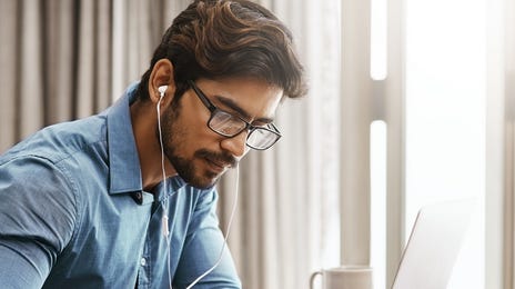 Man with headphones attending an online English course with Berlitz El Salvador from his laptop and taking notes