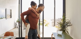 Man giving a piggyback to his daughter indoors looking at Google Nest Hub