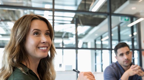 Woman sitting at a table smiling and making notes during an SLE preparation course with Berlitz Canada