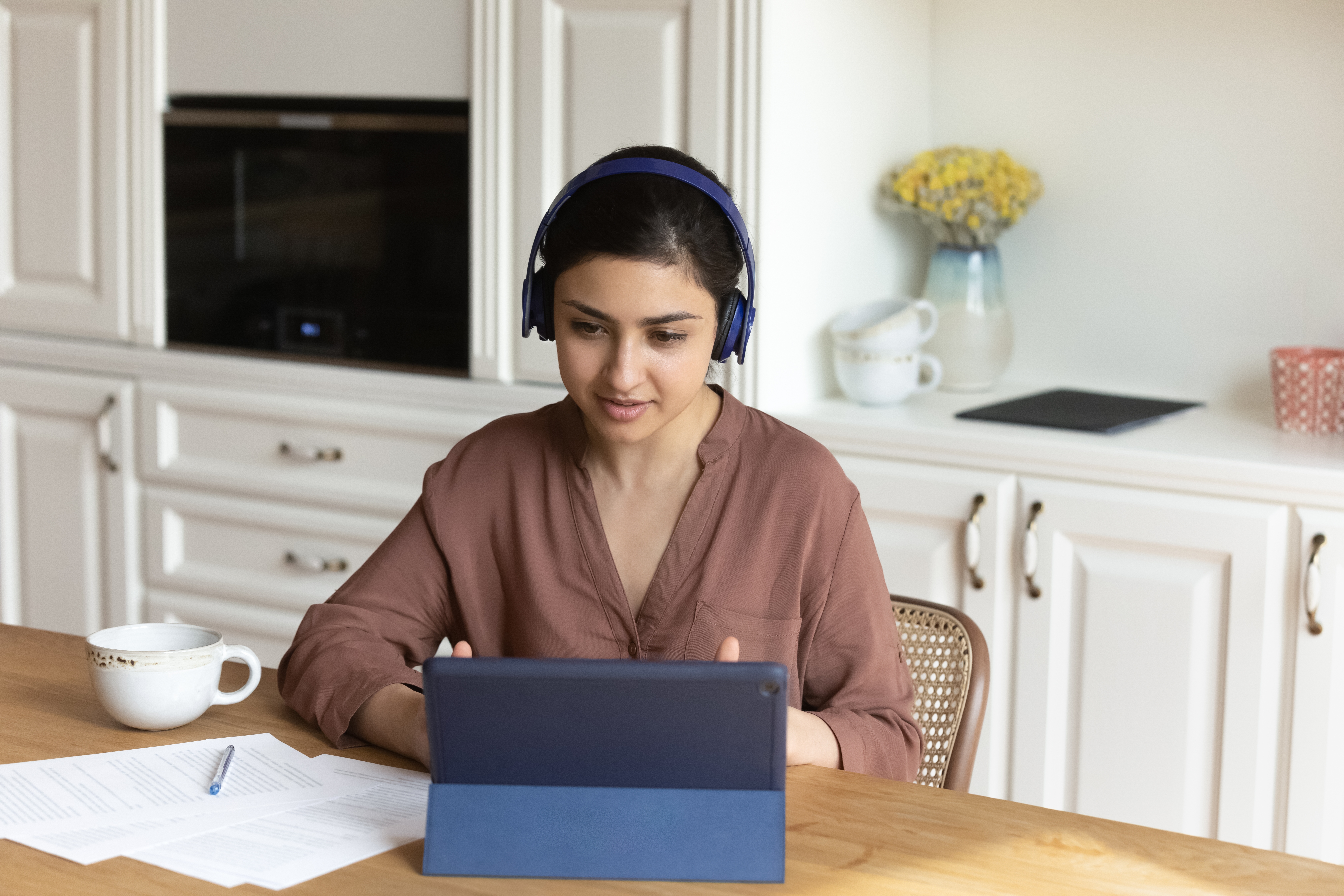 Woman in her kitchen with headphones talking to her instructor during an online intensive language lesson with Berlitz Canada